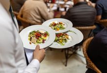 Garçom carrega pratos entre mesas cheias em um restaurante