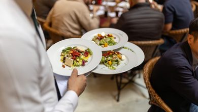 Garçom carrega pratos entre mesas cheias em um restaurante